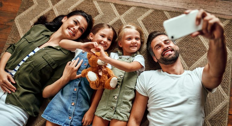 Eine Familie mit Kindern auf Mallorca liegen auf dem Boden machen ein Selfie und fühlen sich gut abgesichert
